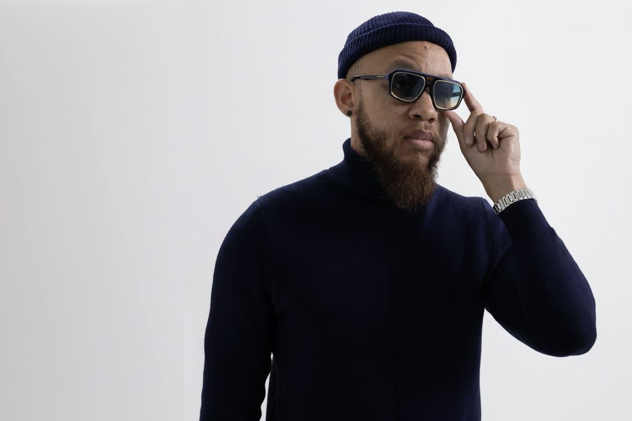 Man wearing a navy sweater, beanie, and sunglasses on a light gray background